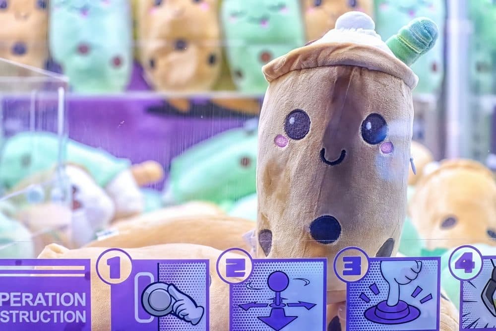 Close-up of a smiling boba tea plush resting against the glass inside a claw machine.