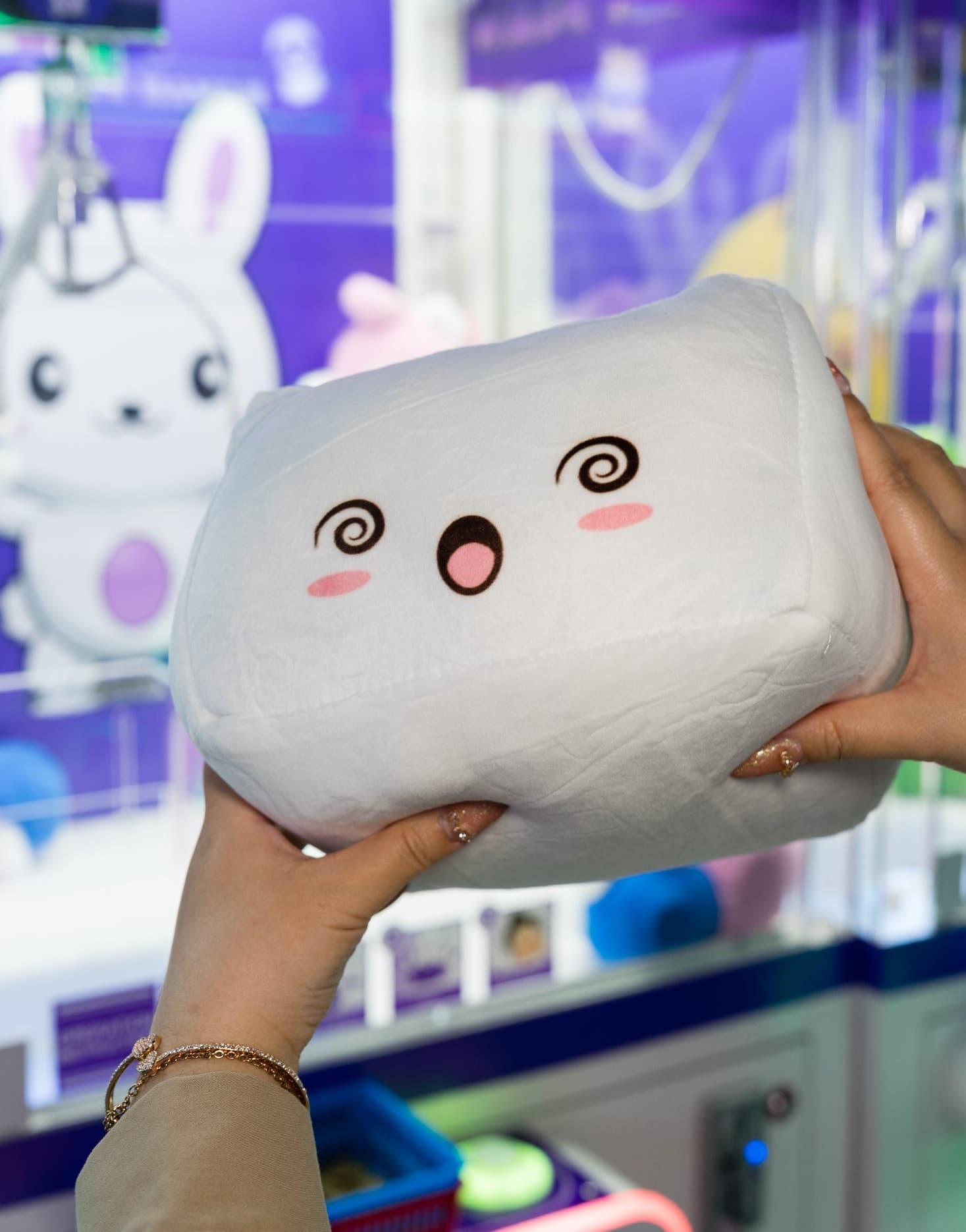 A hand holding up a large white marshmallow plush with a happy face, freshly won.