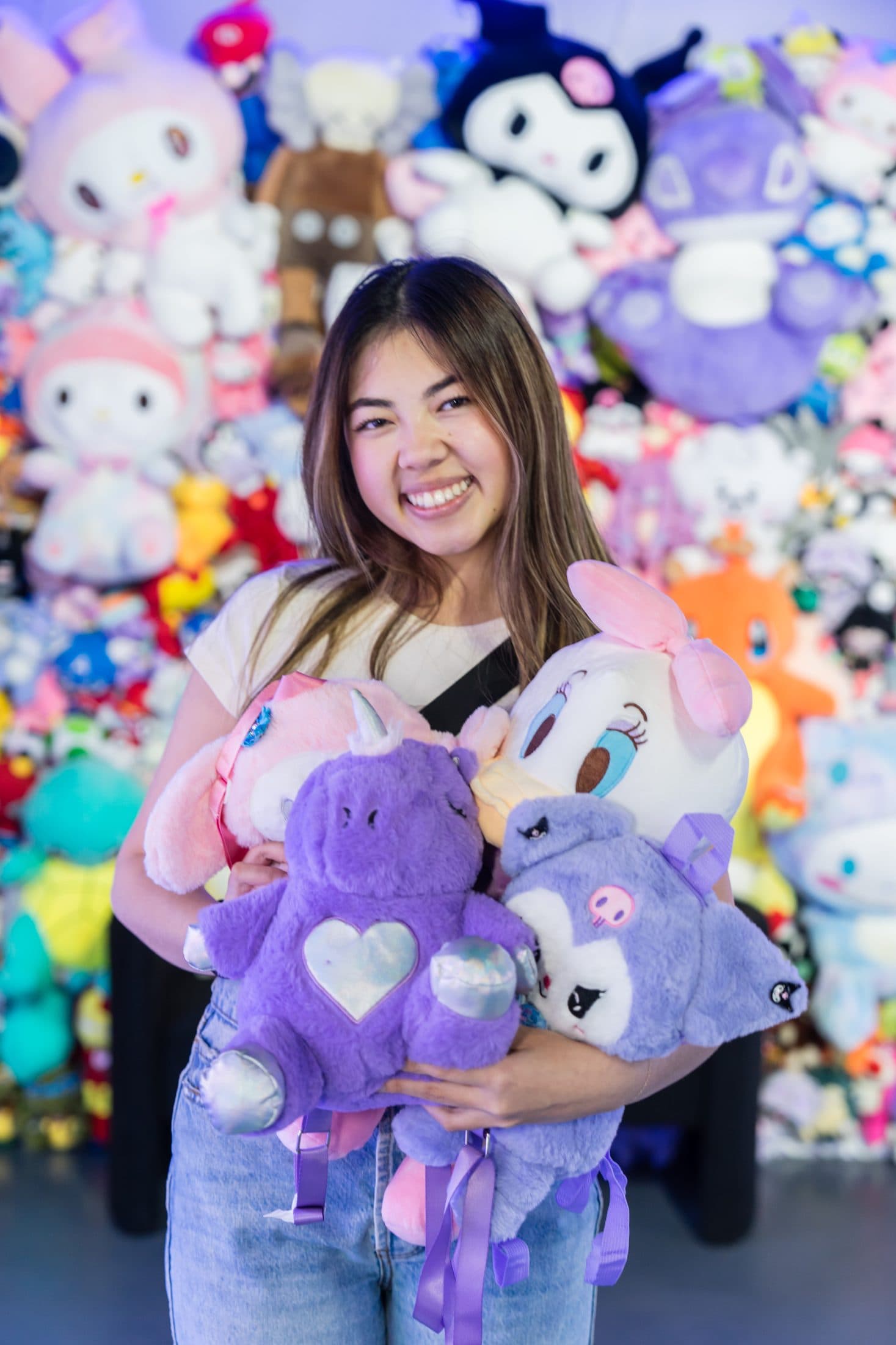 A smiling guest holding an armful of purple plush toys won at the arcade.