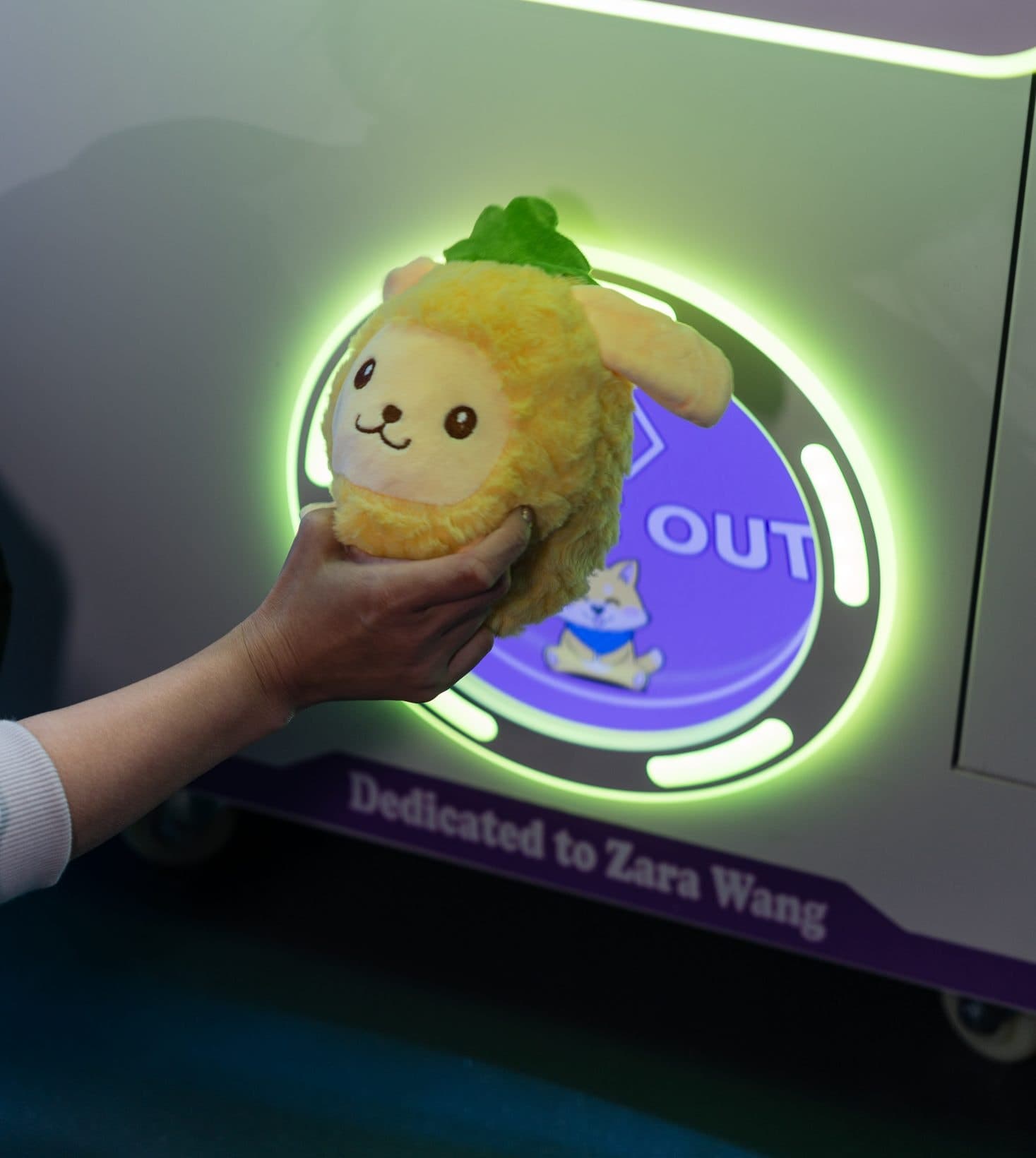 A hand lifting a won plush toy out of the glowing prize door of a claw machine.